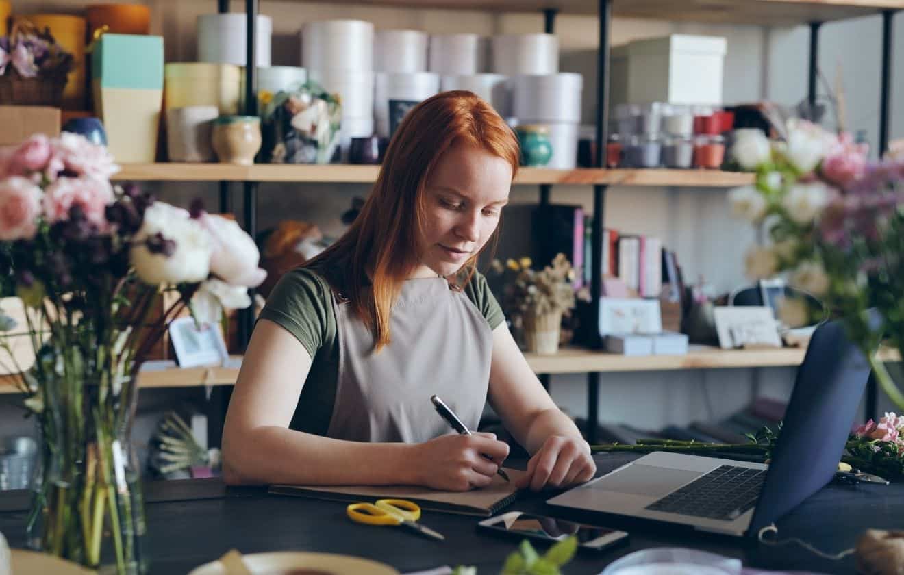 Fleuriste travaillant sur un ordinateur portable dans son atelier floral pour développer son activité et sa présence en ligne.
