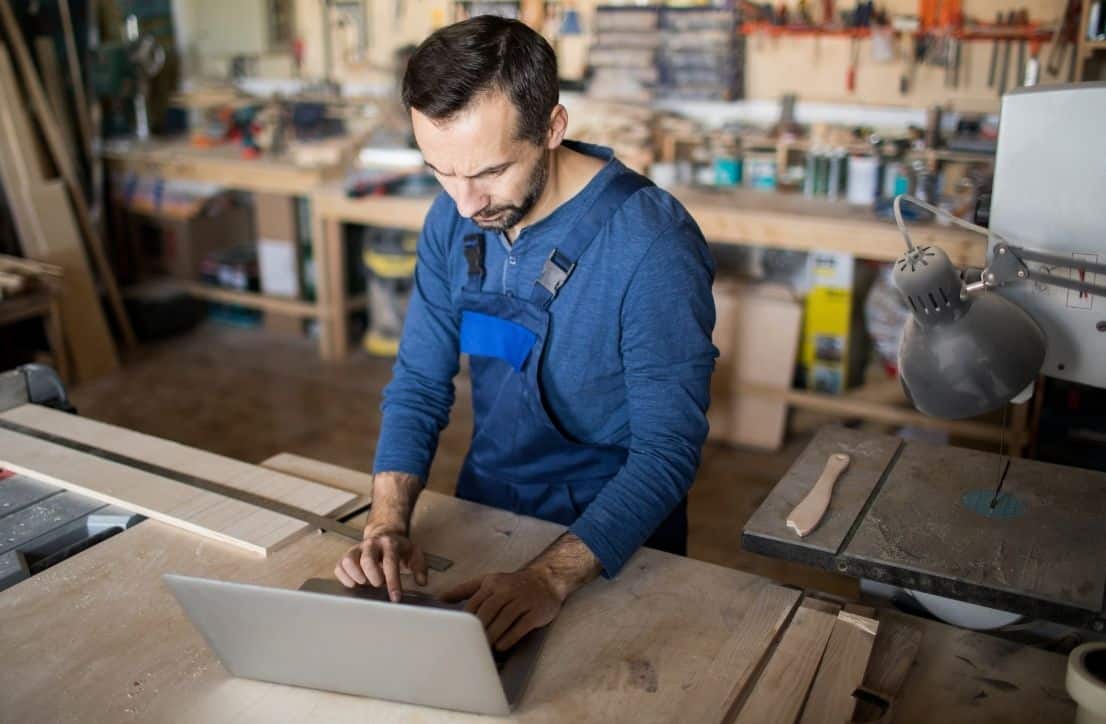 Artisan menuisier utilisant un ordinateur portable dans son atelier pour développer son activité et sa présence en ligne.