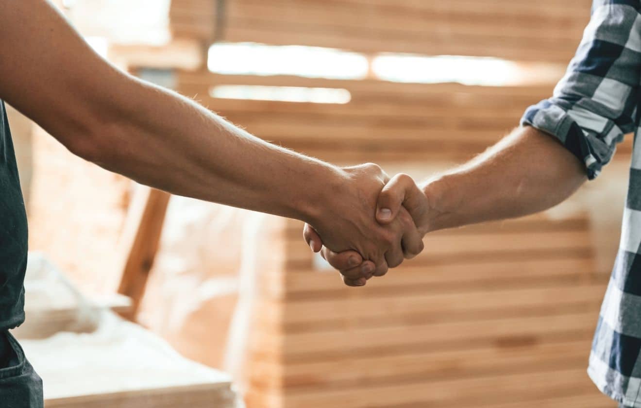 Poignée de main entre un artisan et un client devant un ordinateur portable lors d’un projet de création de site internet.